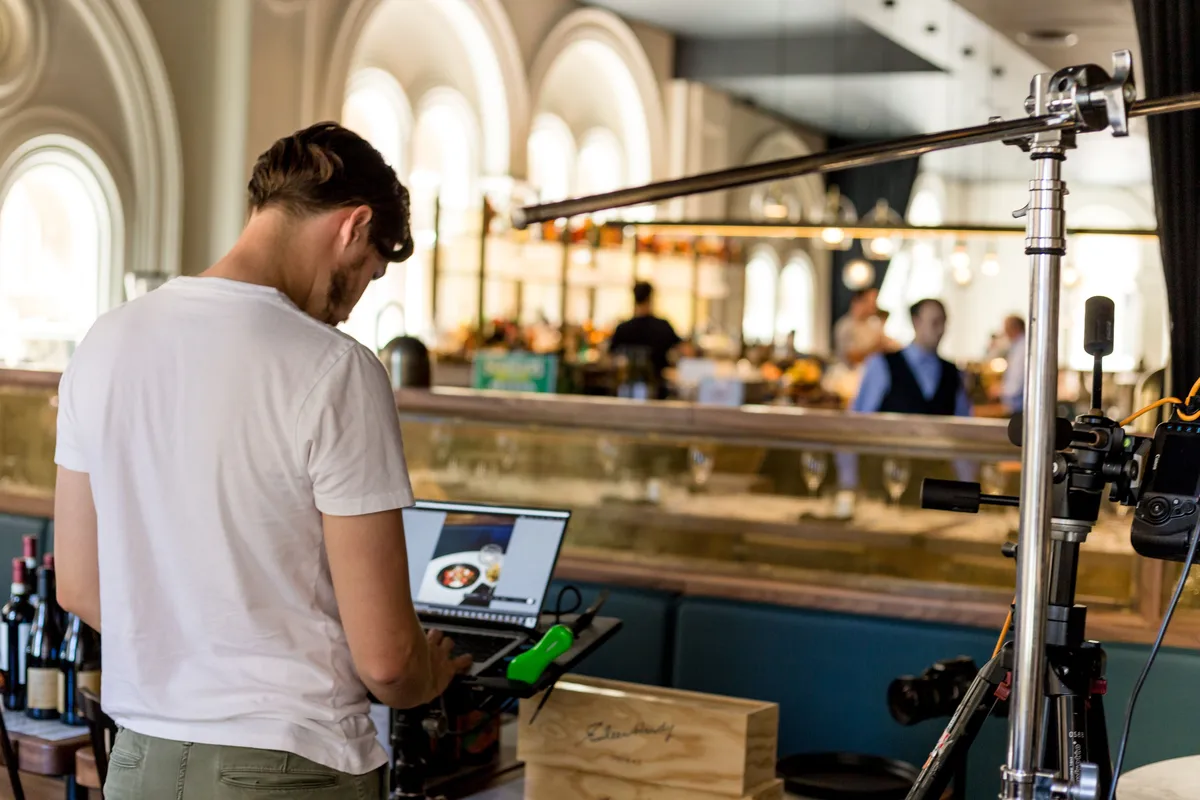 Photographer using laptop and camera equipment in a modern restaurant interior.